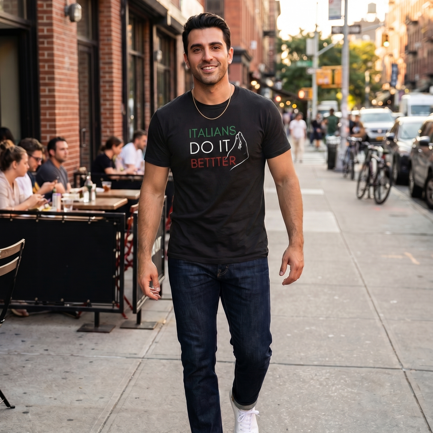 Man wearing a black “Italians Do It Better” graphic t-shirt featuring Italian flag colors while walking through a city street. Stylish Italian heritage shirt celebrating Italian pride, culture, family traditions, and casual everyday fashion.