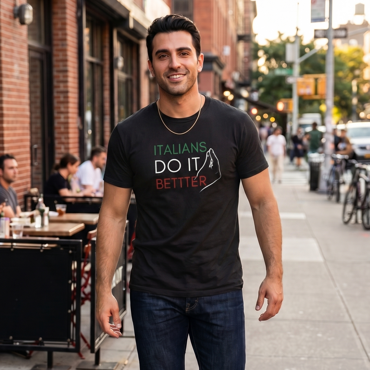 Man wearing a black “Italians Do It Better” graphic t-shirt featuring Italian flag colors while walking through a city street. Stylish Italian heritage shirt celebrating Italian pride, culture, family traditions, and casual everyday fashion.