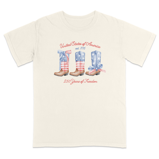 Ivory patriotic graphic tee featuring vintage American flag cowboy boots with “United States of America,” “Est. 1776,” and “250 Years of Freedom” text for a western-inspired Americana look.
