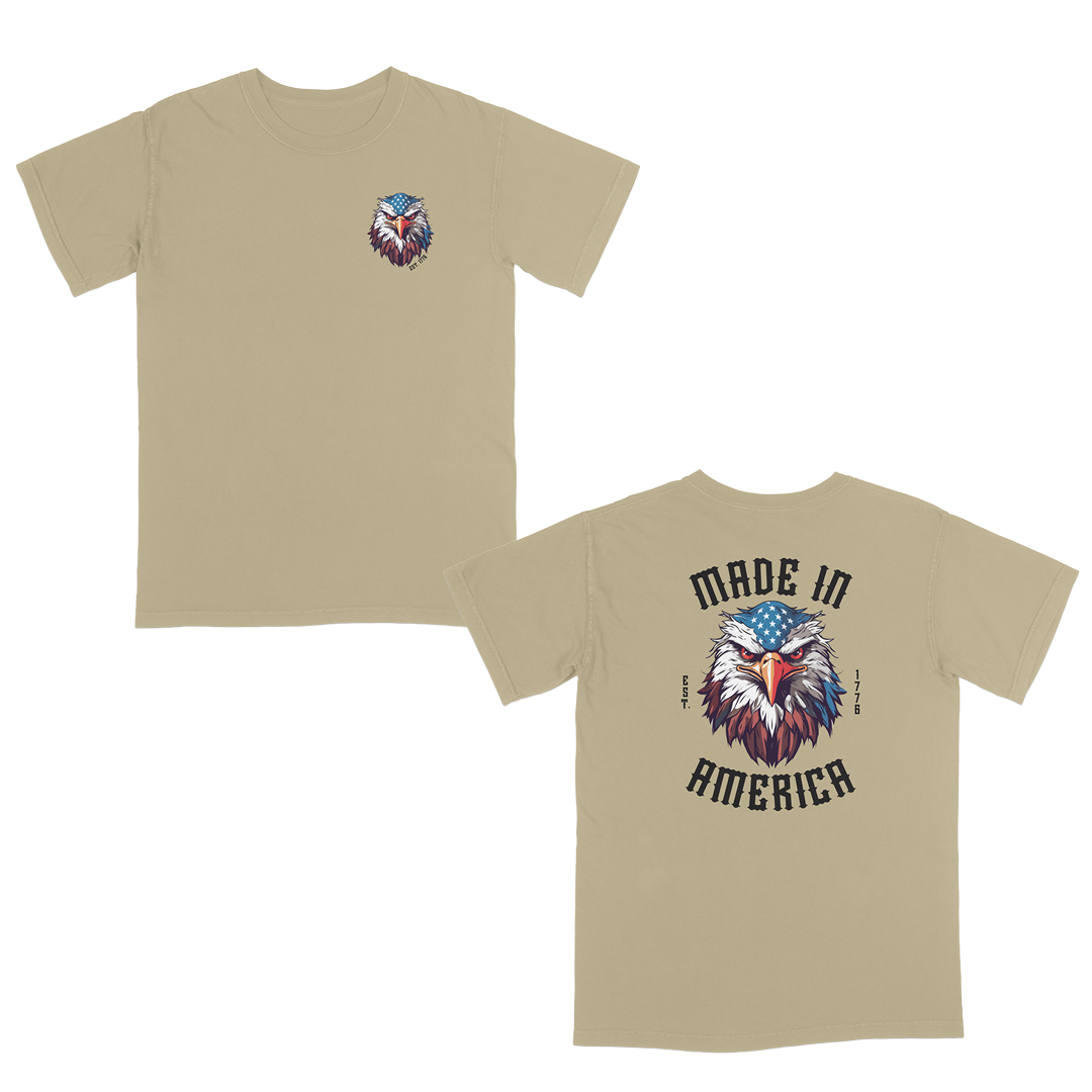 Khaki patriotic graphic tee featuring a fierce bald eagle with an American flag bandana and bold “Made in America” gothic lettering, celebrating classic USA pride and heritage-inspired style.