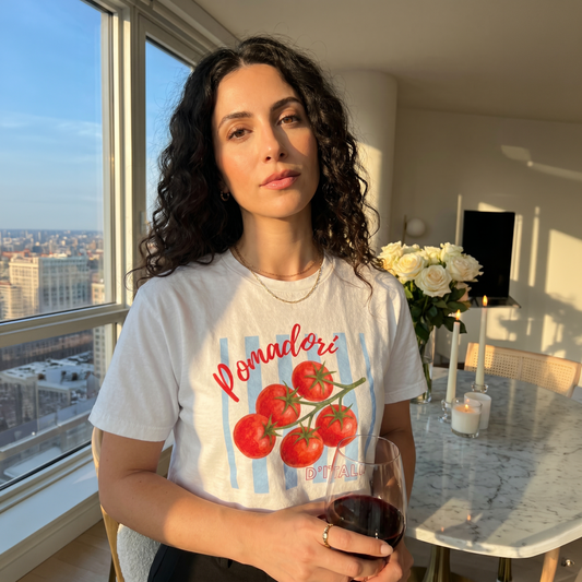 Woman wearing a white “Pomodori d’Italia” graphic t-shirt featuring vibrant tomatoes and vintage Italian-inspired artwork. Stylish Italian heritage shirt celebrating Italian culture, food, family traditions, and Mediterranean lifestyle with a modern casual look.