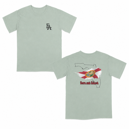 Light sage green short-sleeve T-shirt featuring a minimalist “FLA” logo on the front and a bold back graphic with the outline of Florida, the Florida state flag design, and “Born and Raised” text in red gothic font.