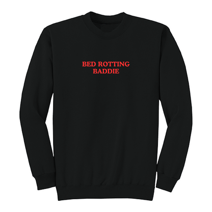 Front view of a black crewneck sweatshirt featuring the phrase "BED ROTTING BADDIE" in small vintage-style red lettering centered on the chest. This minimalist graphic sweatshirt combines cozy comfort with trendy Gen Z-inspired humor, making it perfect for lounging, casual outings, and everyday wear.