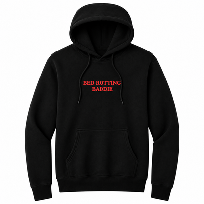 Front view of a black pullover hoodie featuring the phrase "BED ROTTING BADDIE" in small vintage-style red lettering centered on the chest. This minimalist graphic hoodie blends cozy comfort with trendy Gen Z humor, making it perfect for casual lounging and everyday wear.