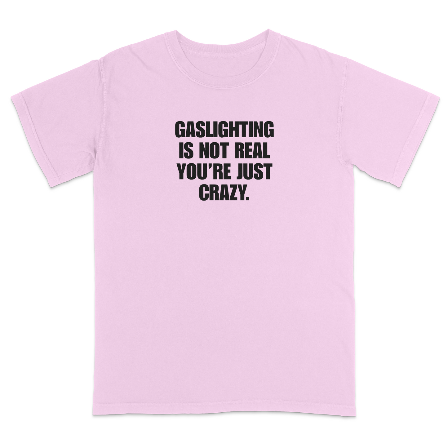 Front view of a light pink short sleeve t-shirt featuring the phrase "GASLIGHTING IS NOT REAL YOU’RE JUST CRAZY." printed in bold black uppercase lettering centered on the chest. The high-contrast black-and-white design creates a clean, minimalist statement tee with a humorous, sarcastic style.