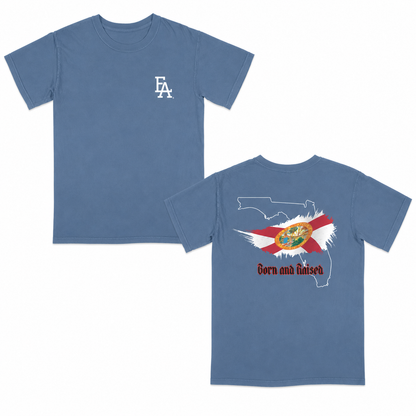 Blue short-sleeve T-shirt featuring a minimalist “FLA” logo on the front and a bold back graphic with the outline of Florida, the Florida state flag design, and “Born and Raised” text in red gothic font.