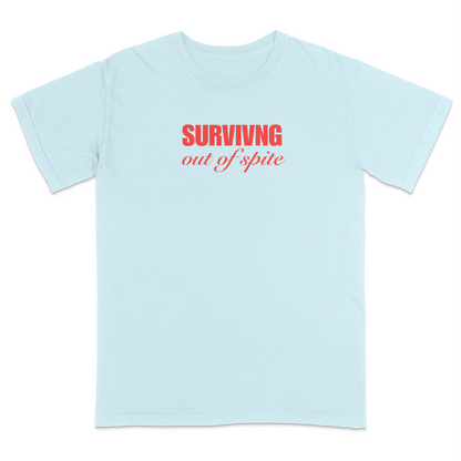 Front view of a chambray short sleeve t-shirt featuring the phrase "SURVIVING" in bold red block letters above the words "out of spite" in elegant red script centered on the chest. The minimalist red-on-black design creates a striking, resilient statement tee with a clean, modern aesthetic.