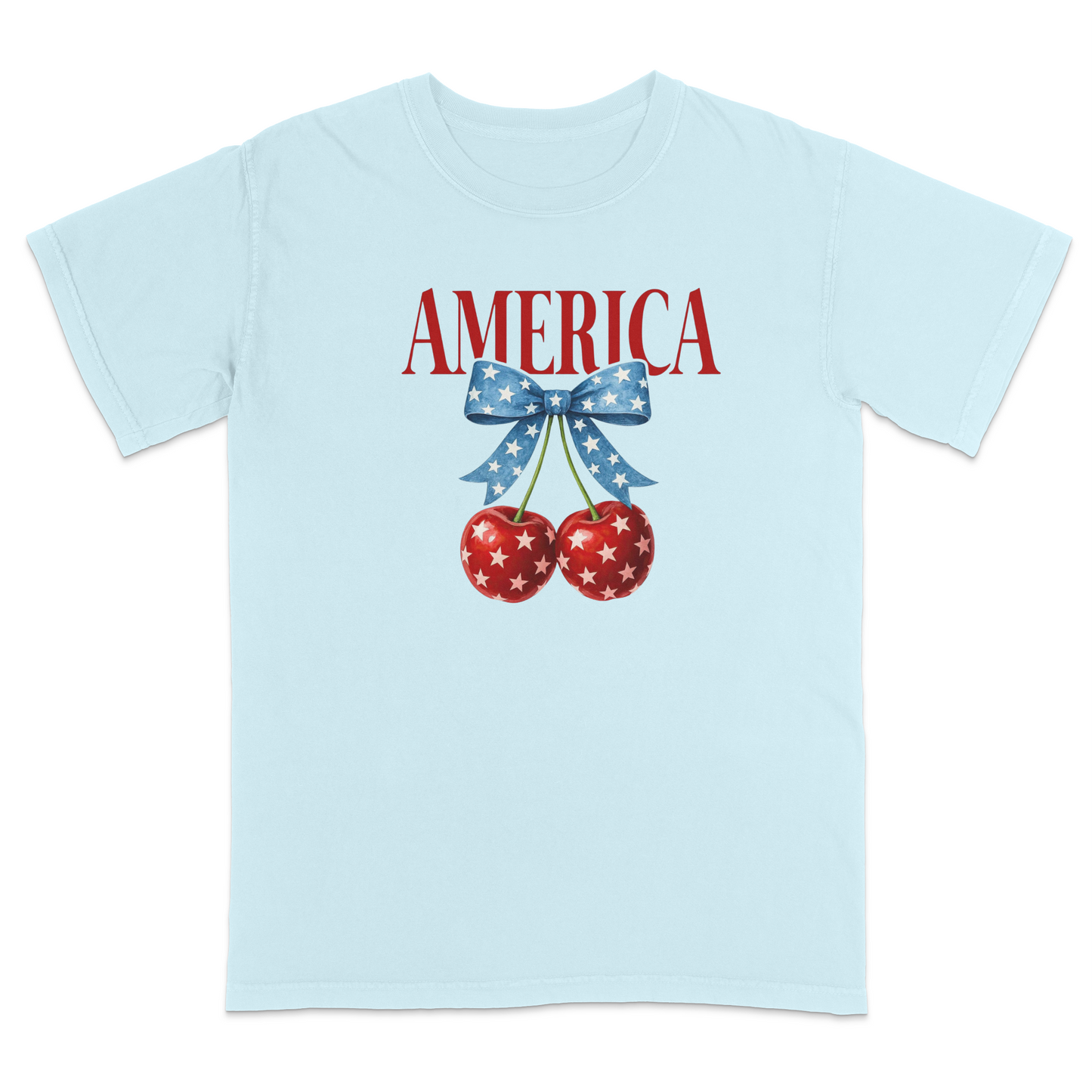 Light Blue patriotic graphic t-shirt featuring red “AMERICA” text with star-pattern cherries and a blue bow design, combining vintage Americana style with playful patriotic fashion.