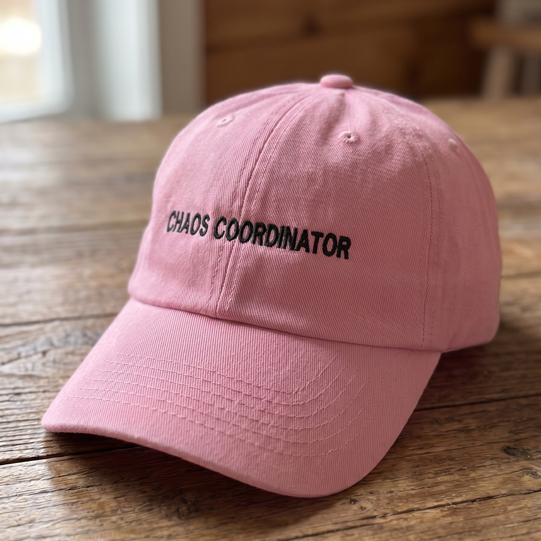 Pink embroidered dad hat featuring the phrase “Chaos Coordinator” in black stitching. Funny mom hat and everyday casual cap with a humorous statement design, perfect for busy parents, teachers, organizers, and gift giving.