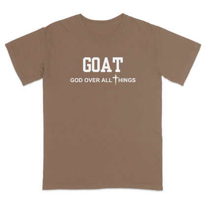 Brown faith-based Christian t-shirt featuring the bold word “GOAT” across the chest with the phrase “God Over All Things” underneath and a white cross graphic. Inspirational religious apparel designed for believers, church events, youth groups, Christian streetwear, Bible study gatherings, and everyday faith-centered fashion.