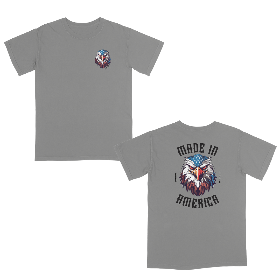 Grey patriotic graphic tee featuring a fierce bald eagle with an American flag bandana and bold “Made in America” gothic lettering, celebrating classic USA pride and heritage-inspired style.