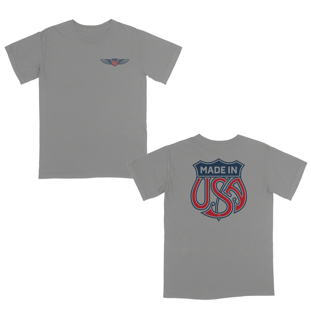 Grey patriotic graphic t-shirt with small USA wing logo on the front and oversized “Made in USA” graphic on the back in vintage red and blue Americana style.