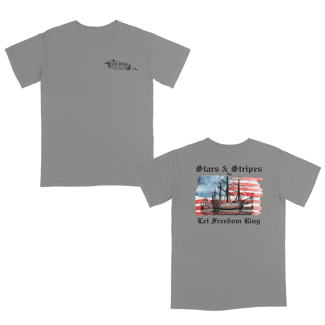Grey patriotic graphic tee featuring a vintage sailing ship over an American flag with “Stars & Stripes” and “Let Freedom Ring” artwork celebrating 250 years of American freedom and heritage.
