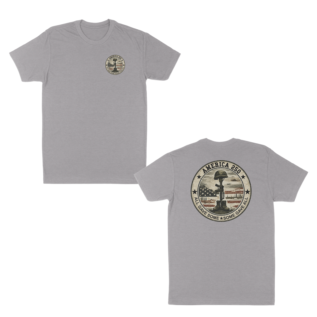 Heather grey patriotic memorial t-shirt featuring a small front chest badge and large back graphic with battlefield cross memorial, distressed American flag, “America 250” design, and “All Gave Some • Some Gave All” tribute text.