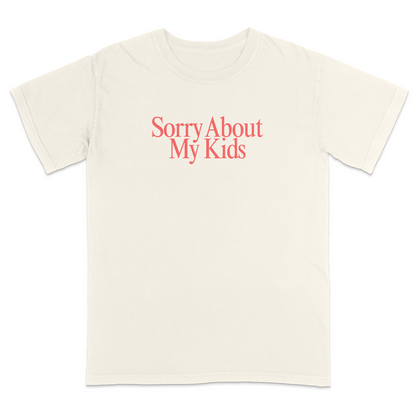 Front view of a ivory graphic T-shirt featuring the phrase "Sorry About My Kids" in large soft pink serif lettering centered across the chest. This minimalist parenting humor tee offers a clean modern design, making it perfect for moms, dads, school events, family outings, playdates, and everyday casual wear.