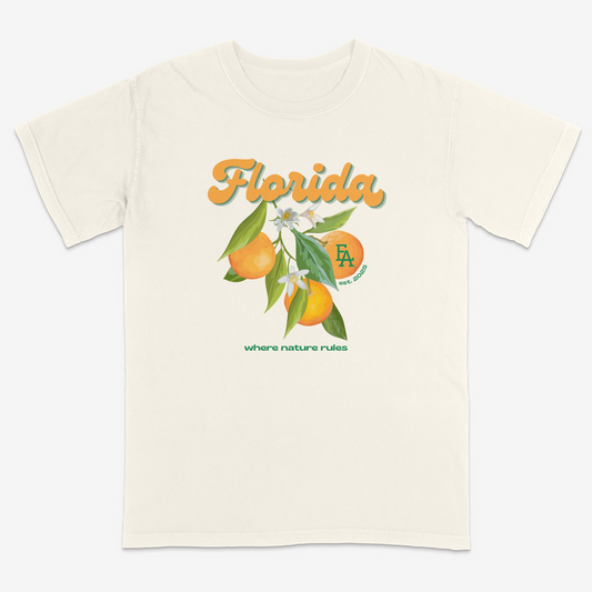 Ivory short-sleeve T-shirt featuring a colorful Florida citrus graphic with oranges, leaves, and blossoms, “Florida” script text, small “FLA est. 2025” logo, and “where nature rules” slogan on the front.