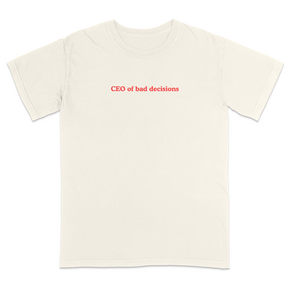 Front view of a ivory graphic T-shirt featuring the phrase "CEO of bad decisions" in small vintage-style red lettering centered on the chest. This minimalist humor tee offers a clean, trendy design that's perfect for casual everyday wear and sarcastic self-expression.
