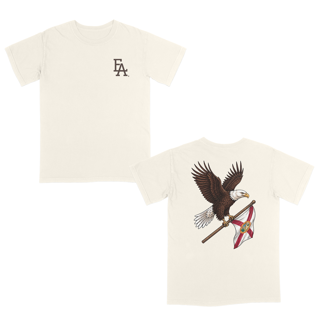 Ivory patriotic t-shirt featuring a small FLA® logo on the left chest and a large back graphic of a soaring bald eagle carrying the Florida state flag. Florida-inspired apparel combining state pride, American heritage, and outdoor lifestyle style. Perfect for patriotic events, fishing trips, hunting, boating, beach days, and everyday Florida living.