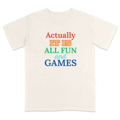 Front view of a ivory graphic T-shirt featuring the phrase "Actually It Is All Fun and Games" in bold multicolored lettering, with "Actually" in red, "IT IS" in gold, "ALL FUN" in green, "and" in light blue script, and "GAMES" in blue. This colorful humorous graphic tee has a playful retro-inspired design, making it perfect for casual wear, parties, game nights, and everyday outfits.