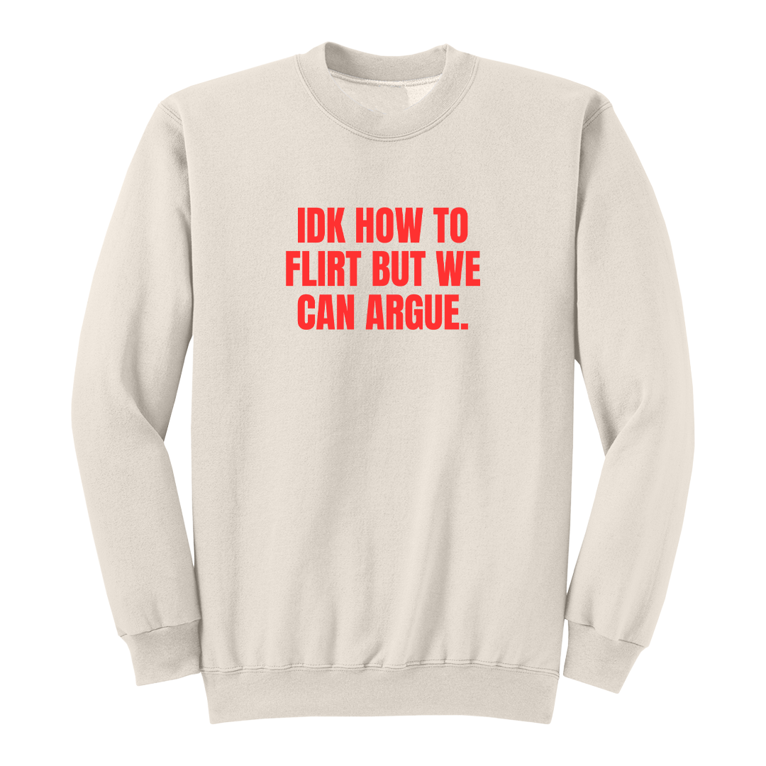 Front view of a natural long sleeve graphic crewneck featuring the bold red statement "IDK HOW TO FLIRT BUT WE CAN ARGUE." centered across the chest in large uppercase block lettering. This funny sarcastic long sleeve shirt combines relationship humor with bold typography, making it a casual streetwear piece for adults with a playful sense of humor.
