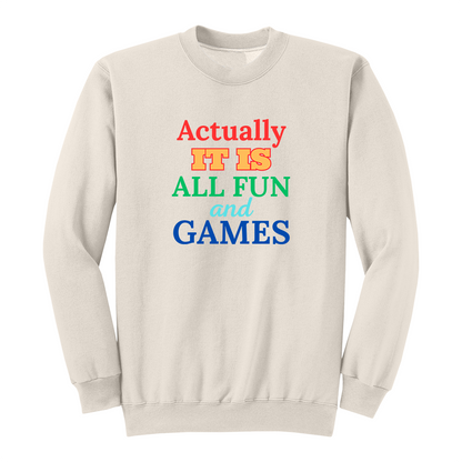 Front view of a natural long sleeve graphic T-shirt featuring the phrase "Actually IT IS ALL FUN and GAMES" in stacked multicolored typography. "Actually" is red, "IT IS" is gold with a red outline, "ALL FUN" is green, "and" is written in light blue script, and "GAMES" is bold blue. This playful retro-inspired graphic long sleeve shirt is perfect for casual wear, parties, game nights, and anyone with a fun sense of humor.
