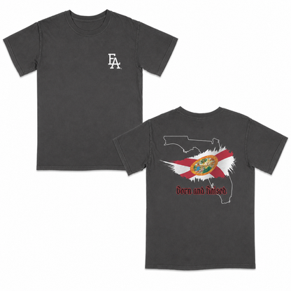 Dark Grey short-sleeve T-shirt featuring a minimalist “FLA” logo on the front and a bold back graphic with the outline of Florida, the Florida state flag design, and “Born and Raised” text in red gothic font.