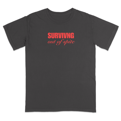 Front view of a pepper short sleeve t-shirt featuring the phrase "SURVIVING" in bold red block letters above the words "out of spite" in elegant red script centered on the chest. The minimalist red-on-black design creates a striking, resilient statement tee with a clean, modern aesthetic.