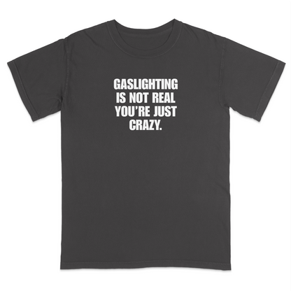 Front view of a pepper short sleeve t-shirt featuring the phrase "GASLIGHTING IS NOT REAL YOU’RE JUST CRAZY." printed in bold white uppercase lettering centered on the chest. The high-contrast black-and-white design creates a clean, minimalist statement tee with a humorous, sarcastic style.