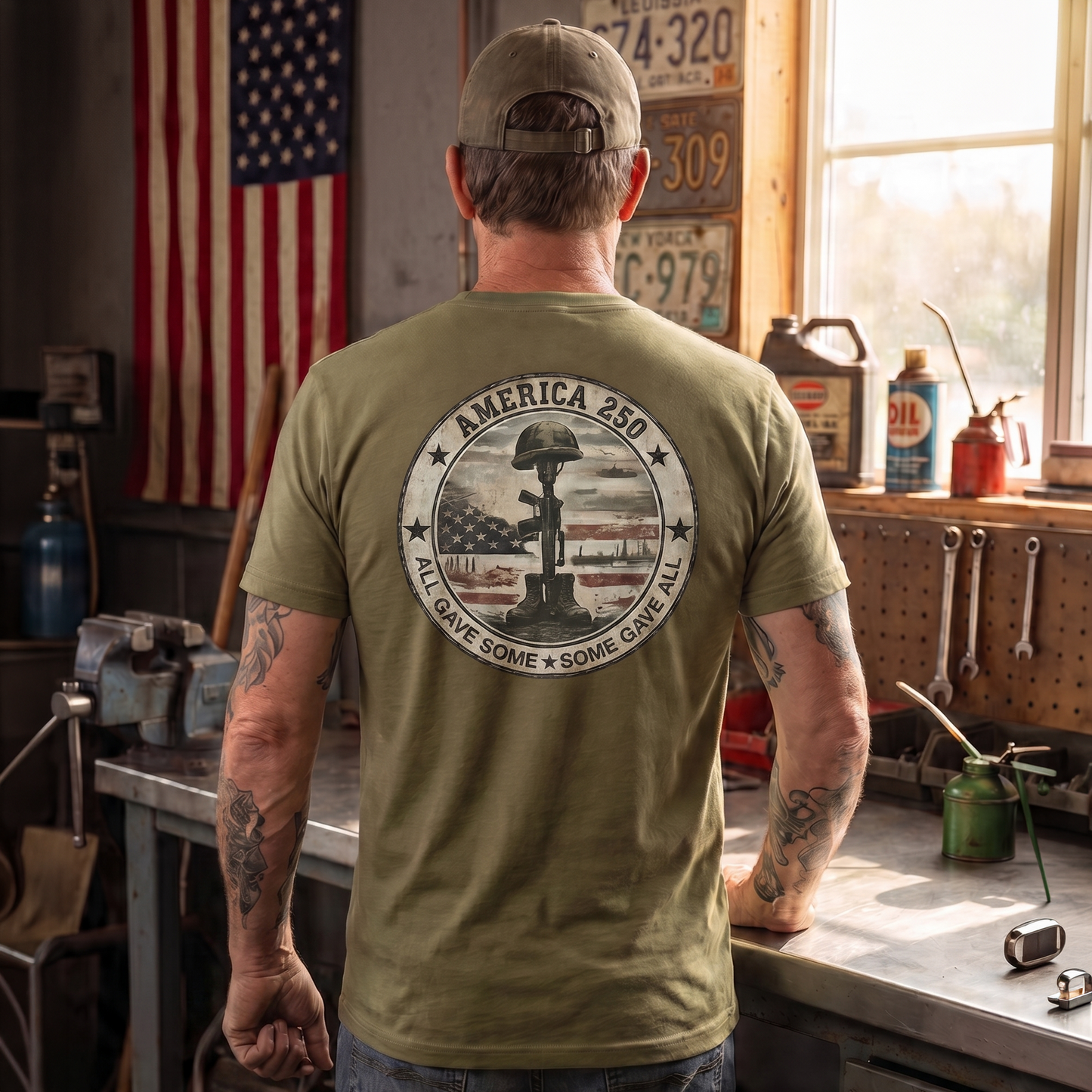 Man wearing an military green patriotic “America 250” graphic t-shirt featuring a battlefield cross memorial with helmet, rifle, and boots inside a vintage American flag design. Patriotic apparel honoring fallen heroes, military service, veterans, sacrifice, and America’s 250th anniversary with the phrase “All Gave Some, Some Gave All.”
