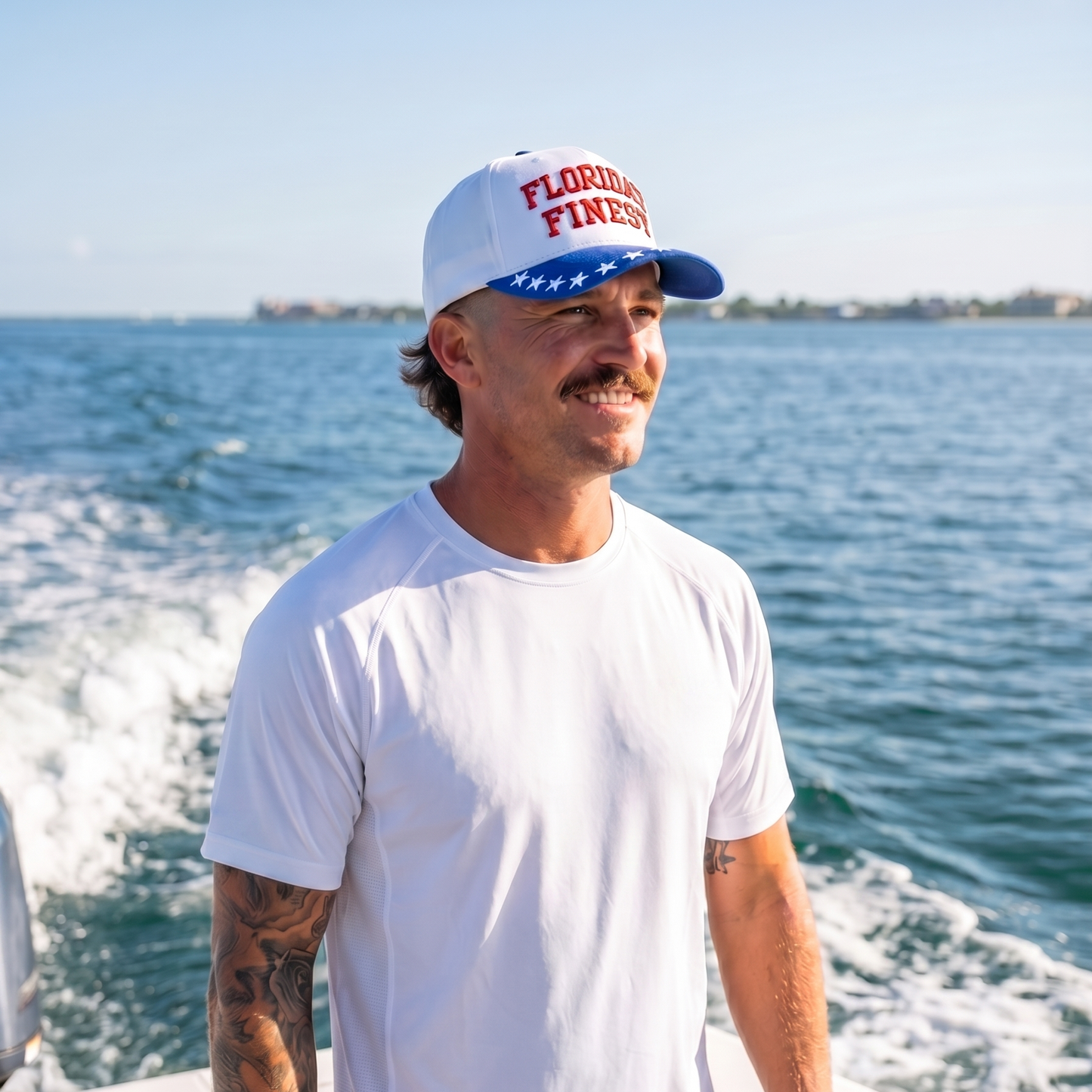 Man wearing a Florida’s Finest embroidered snapback hat with a white crown, red lettering, and blue star-pattern brim while boating on open water. Patriotic Florida lifestyle cap designed for fishing, boating, beach days, and coastal outdoor adventures.