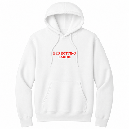 Front view of a white pullover hoodie featuring the phrase "BED ROTTING BADDIE" in small vintage-style red lettering centered on the chest. This minimalist graphic hoodie blends cozy comfort with trendy Gen Z humor, making it perfect for casual lounging and everyday wear.