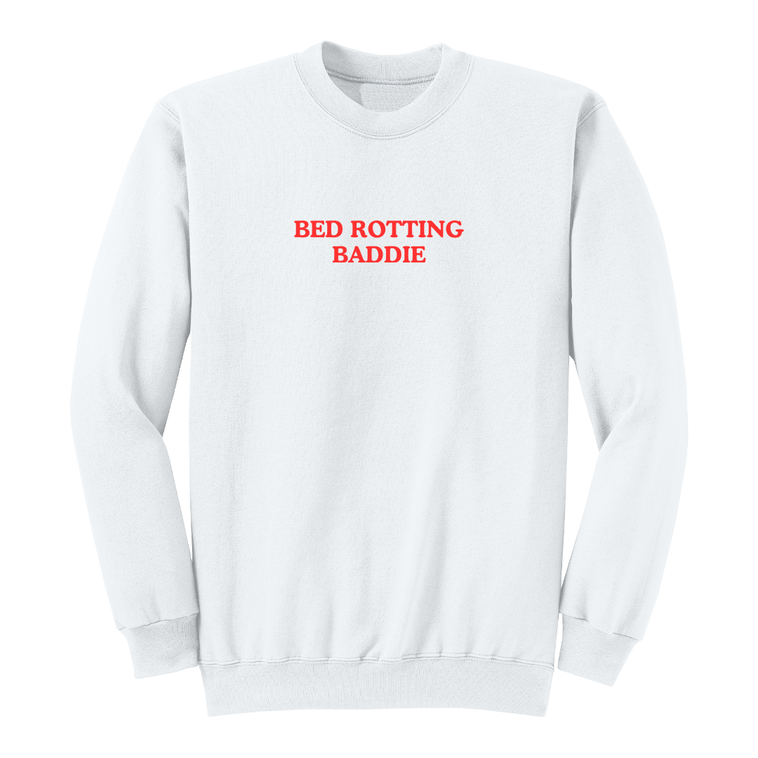 Front view of a white crewneck sweatshirt featuring the phrase "BED ROTTING BADDIE" in small vintage-style red lettering centered on the chest. This minimalist graphic sweatshirt combines cozy comfort with trendy Gen Z-inspired humor, making it perfect for lounging, casual outings, and everyday wear.