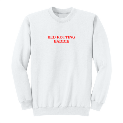 Front view of a white crewneck sweatshirt featuring the phrase "BED ROTTING BADDIE" in small vintage-style red lettering centered on the chest. This minimalist graphic sweatshirt combines cozy comfort with trendy Gen Z-inspired humor, making it perfect for lounging, casual outings, and everyday wear.