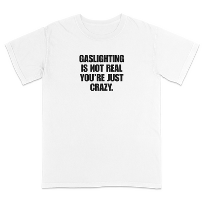 Front view of a white short sleeve t-shirt featuring the phrase "GASLIGHTING IS NOT REAL YOU’RE JUST CRAZY." printed in bold black uppercase lettering centered on the chest. The high-contrast black-and-white design creates a clean, minimalist statement tee with a humorous, sarcastic style.