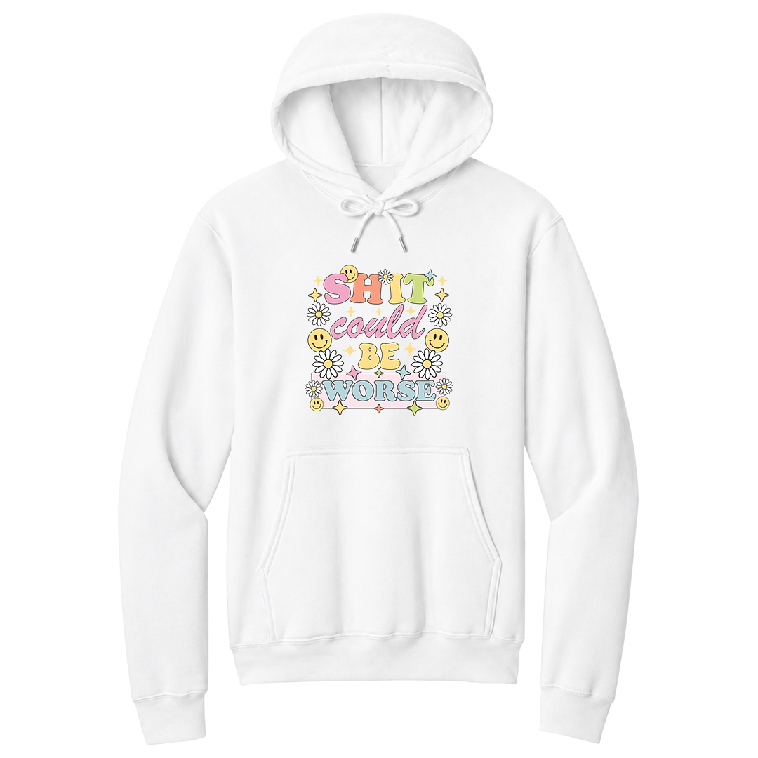 Front view of a white pullover hoodie featuring a colorful retro-inspired graphic with the phrase "SHIT could BE WORSE" in playful pastel typography. The design is surrounded by white daisies, yellow smiley faces, and sparkling star accents, creating a cheerful vintage aesthetic that humorously contrasts with the sarcastic message. The drawstrings are tied into a short bow above the design for a realistic product mockup. A funny adult hoodie with bold humor, retro floral graphics, and casual style