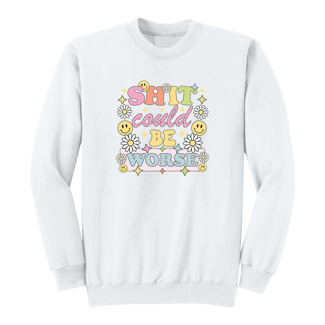 Front view of a white long sleeve graphic shirt featuring a colorful retro-inspired design with the phrase "SHIT could BE WORSE" in playful pastel typography. The graphic is surrounded by white daisies, yellow smiley faces, and sparkling star accents, creating a cheerful vintage aesthetic that humorously contrasts with the sarcastic message. A funny adult long sleeve shirt with retro floral graphics, bold humor, and casual streetwear style.