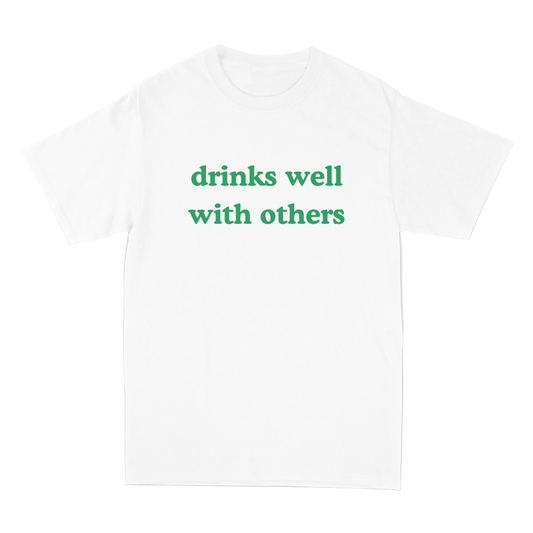 White t-shirt with green text 'drinks well with others' on a light gray background