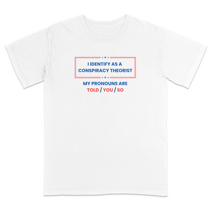 Front view of a white graphic T-shirt featuring the humorous phrase "I Identify as a Conspiracy Theorist" with "My Pronouns Are Told / You / So" printed below in bold patriotic red and blue lettering with stars and a bordered design. A funny political humor tee perfect for casual wear, parties, holidays, and anyone who enjoys satire and conspiracy-themed jokes.