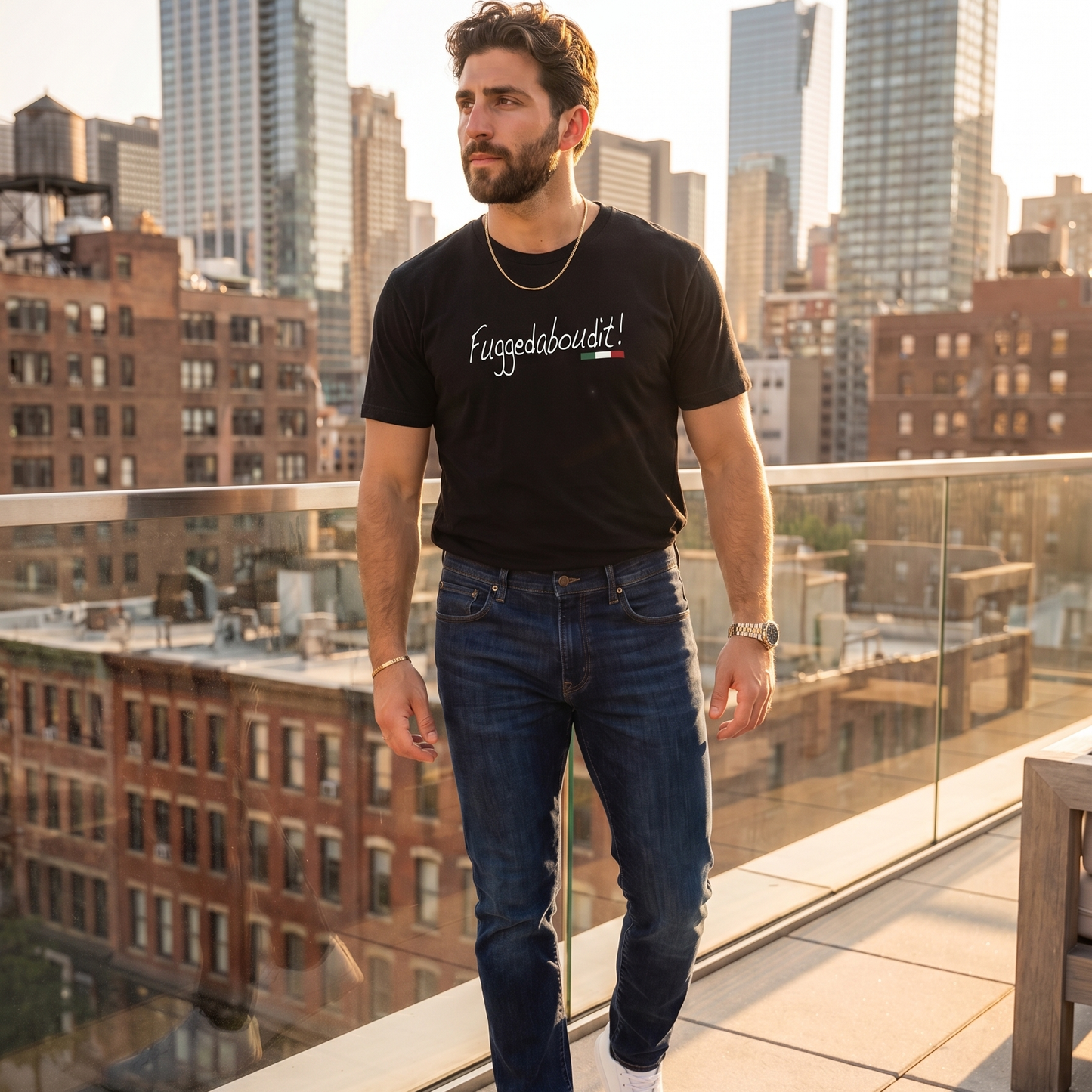 Man wearing a black “Fuggedaboutit!” graphic t-shirt with Italian flag accent, standing on a rooftop overlooking a city skyline. Stylish Italian heritage shirt featuring a classic Italian expression, perfect for Italian pride, family gatherings, and casual everyday wear.